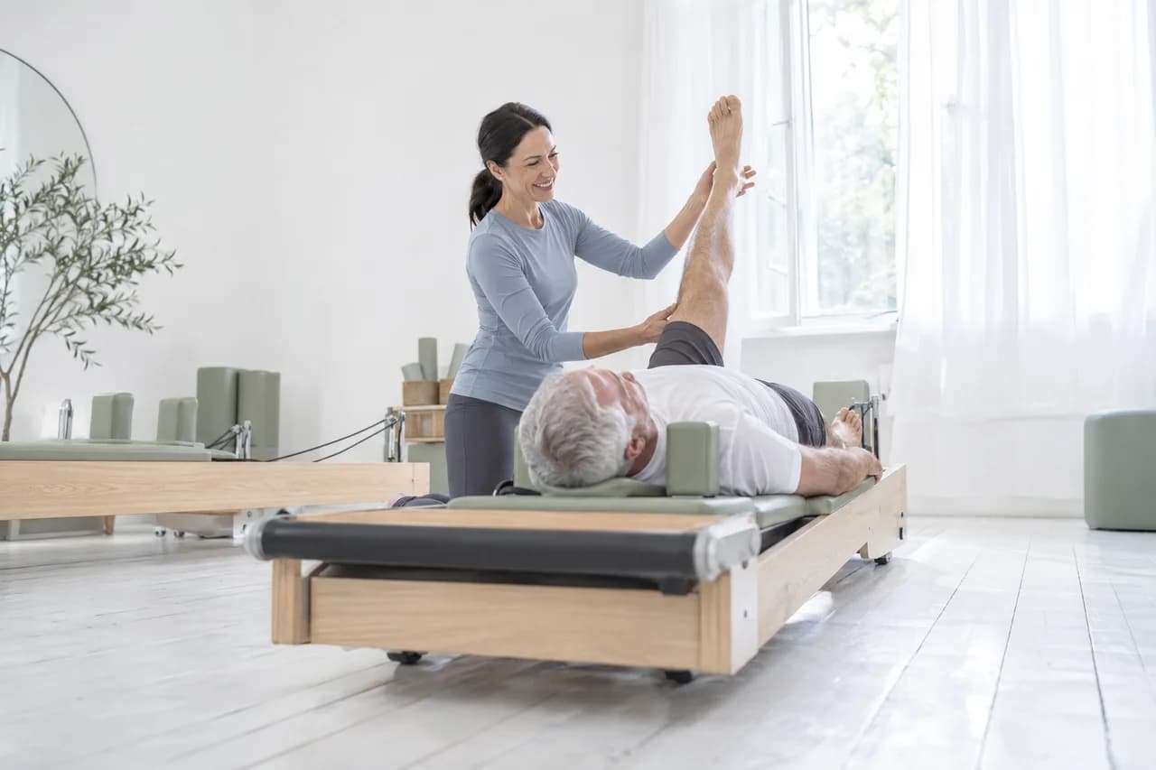 The owner of an invented pilates studio guiding a client's leg on a reformer